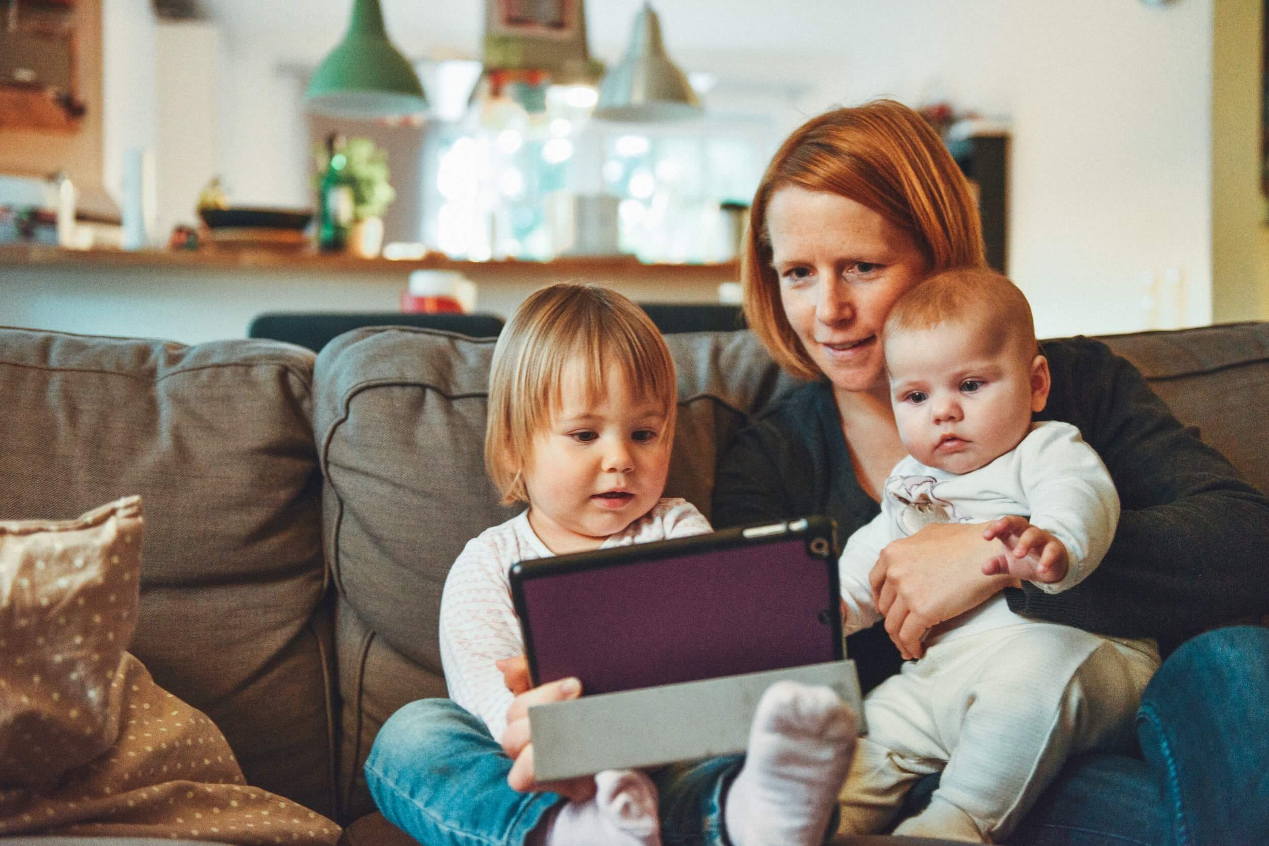 Mom on the couch with two children engaging in parent-teacher communication on a tablet.